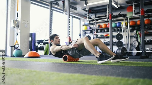 Young fit man in gym doing exercise with foam roller. photo