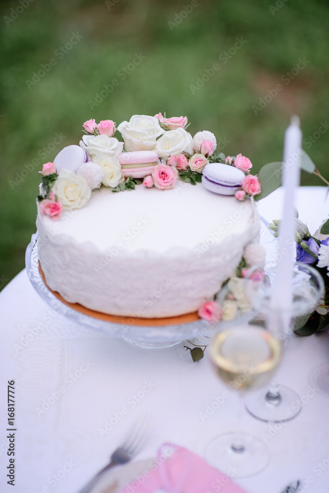 Pretty cake with macaroons and roses stands on the table