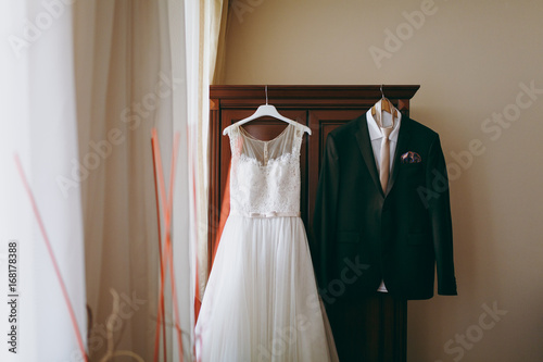 Wedding dress of the bride and groom's suit hang in the room