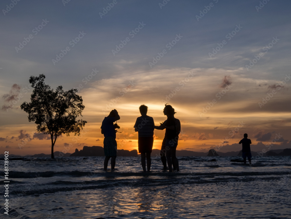 Silhoettes of people enjoying the sunset on the beach in tropical country, Krabi, Thailand.