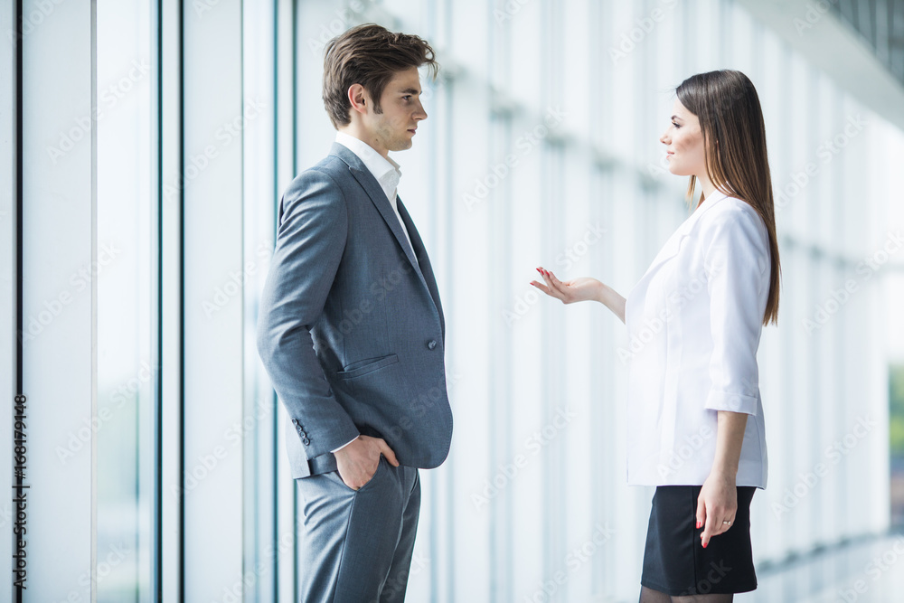 two young businessman and business woman are standing in modern office with panoramic windows.