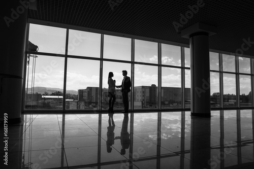 silhouette of Businessman and Businesswoman shaking hands in office with big panoramic windows, Business concept.