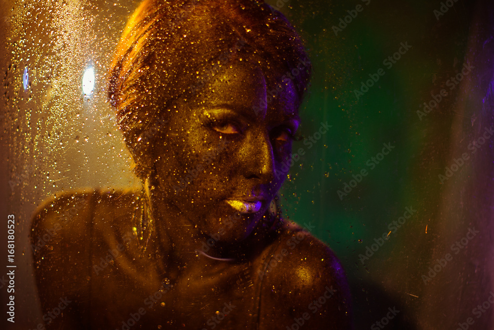 Look through the wet glass at a woman covered with bronze paint