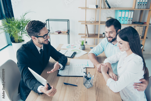 Side profile high angle shot of a deal between married couple and a salesman, consultating them about buying a purchase, all are dressed in formal outfits, smiling photo