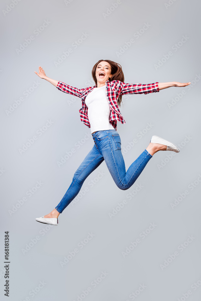I can fly! Happiness, dream, fun, joy concept. Very excited happy cute brunette girl is jumping up, wearing casual clothes, white shoes, on pure light blue background, amazed