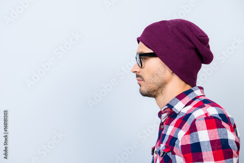 Profile side photo of young serious hipster guy in hat, glasses, with stubble, in casual outfit on pure blue background near the copy space, harsh and brutal © deagreez