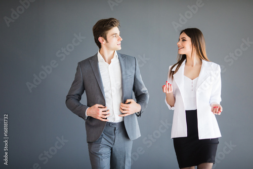 Smiling businesswoman and businessman are conversing against grey background. Business concept. photo