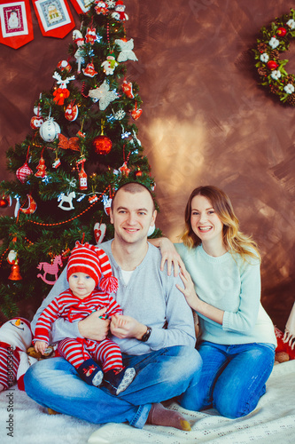 Young parents sit with their little child before a Christmas tree © pyrozenko13