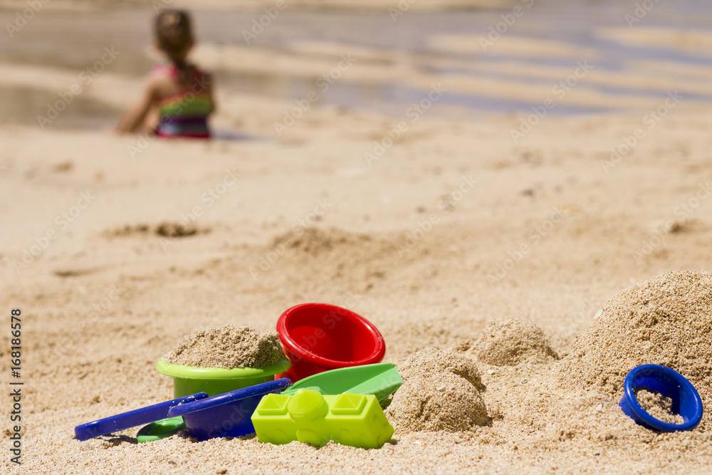 Plastic toys in sand / Colorful plastic toys in the beach with the child on background Plastic toys in sand / Colorful plastic toys in the beach with the child on background