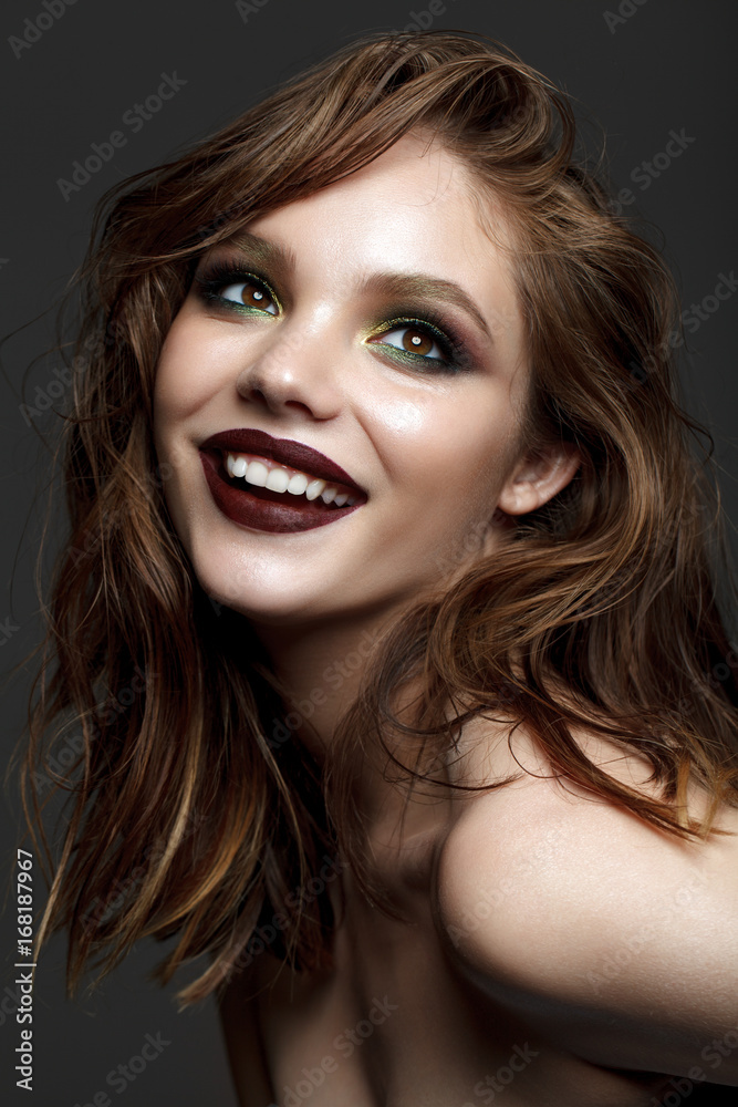 Beautiful smiling young model with evening makeup and wavy hairstyle. Green smoky eyes and wine lips. Trendy hairstyle. Healthy white teeth