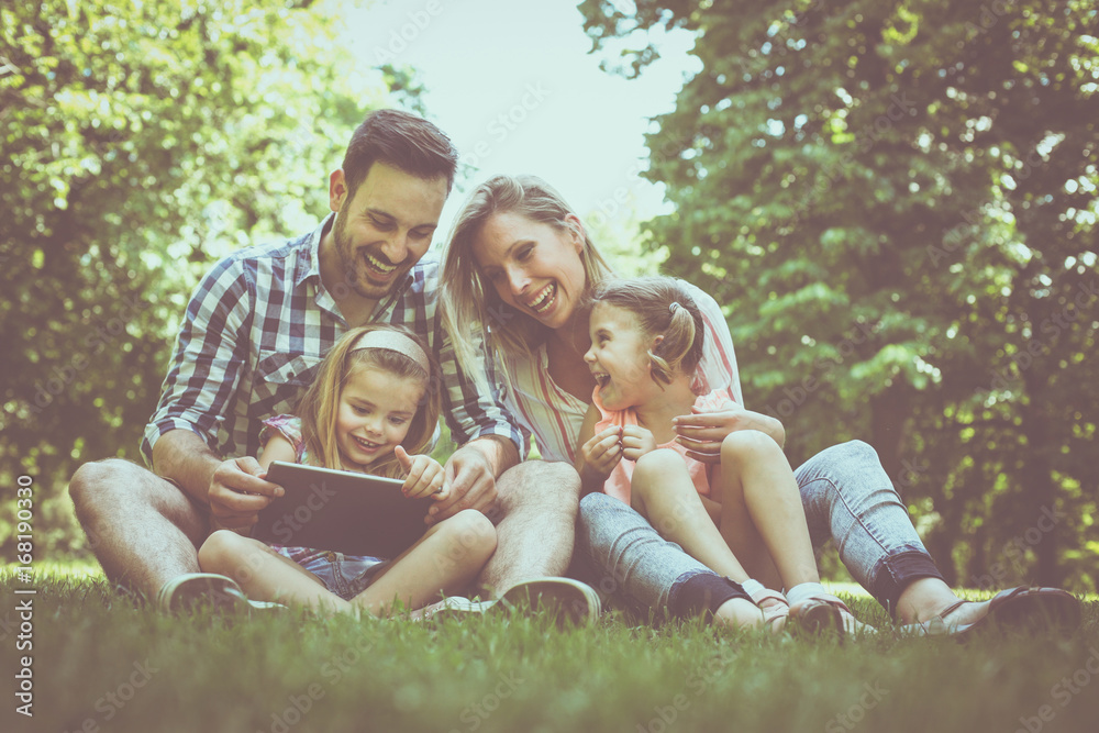 Fototapeta premium Happy family with two children in meadow using digital tablet together. Family in meadow.
