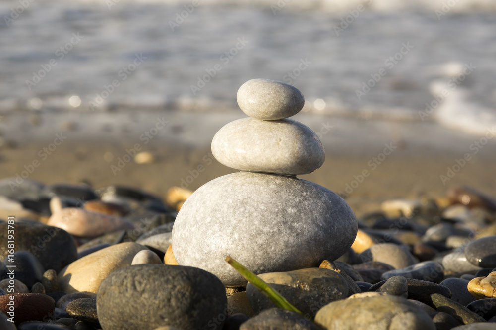 White three pebble cairn on the beach, sunlight White three pebble cairn on the beach, sunlight