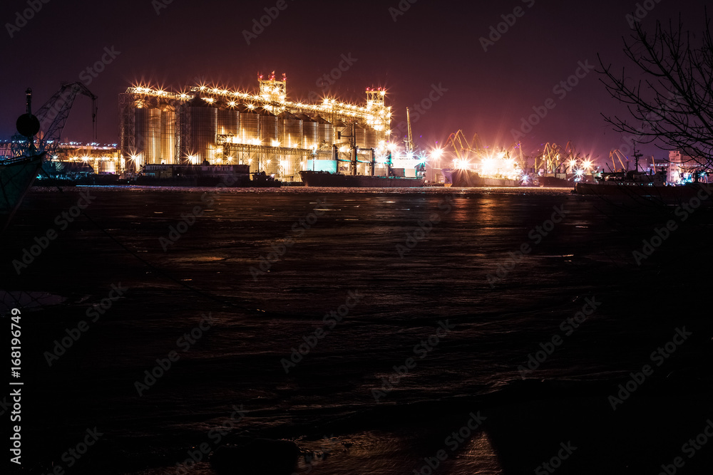 Panorama image of the illuminated cargo port at night, cargo ships and cranes