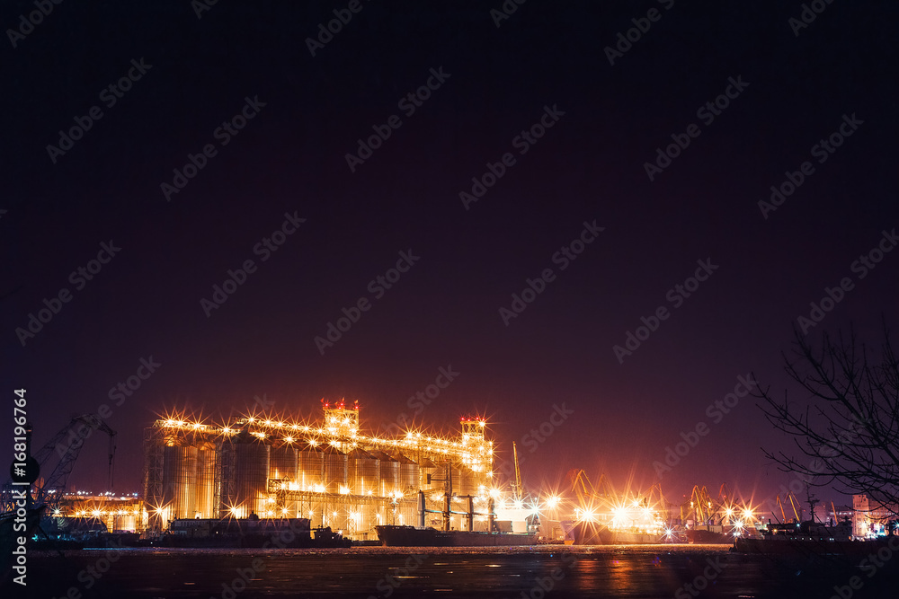 Panorama image of the illuminated cargo port at night, cargo ships and cranes