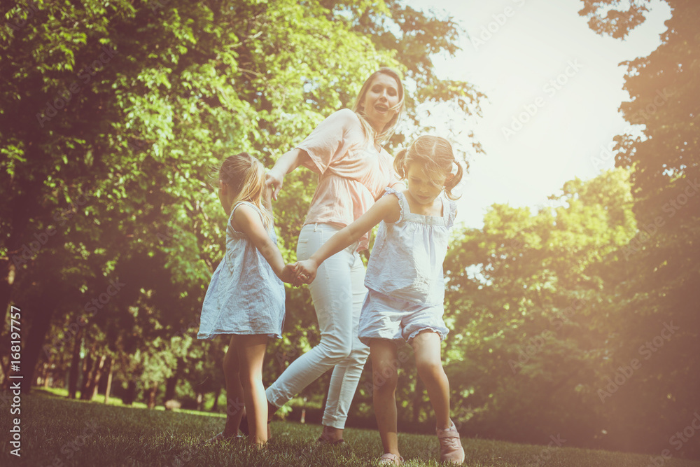 Fototapeta premium Mother playing on meadow with her two little daughter.