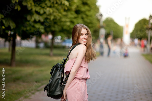 Young beautiful stylishly dressed girl with beautiful hair is walking along the streets of the city at sunset, in sunny rays