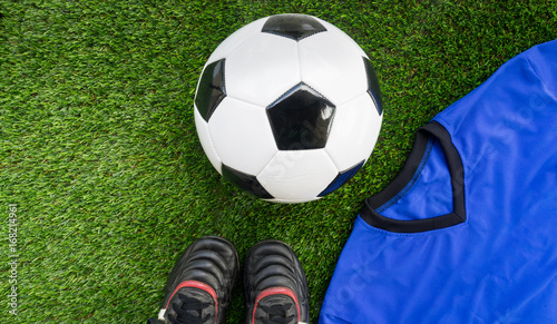 Soccer concept : Football (soccer ball), old soccer boots, blue soccer kit (t-shirt)  on green grass background. Flat lay with copy space.