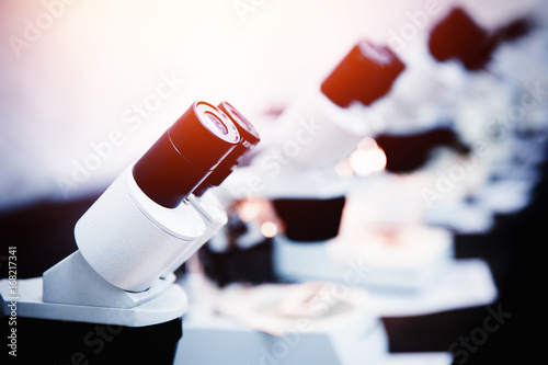 A row of microscopes stands in a room background. Concept medicine, biology, research, education. With a glare of sunlight