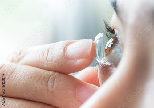 Young asian woman putting contact lens in her right eye, close up