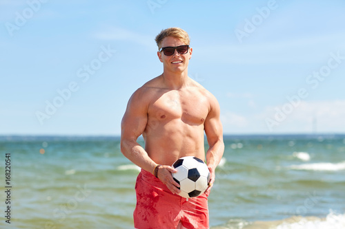 young man with soccer ball on beach