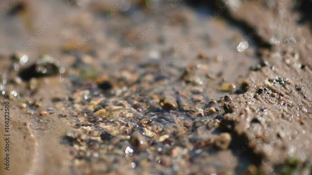 Clean water stream flows through the sand and glare in the sun. Close up. Selective focus. slow motion. Clean water stream flows through the sand and glare in the sun. Close up. Selective focus. slow motion.