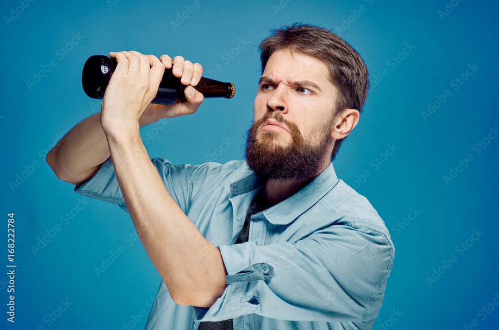 Fototapeta premium Man with a beard on a blue background holds a bottle of beer, portrait, alcohol