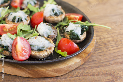 Cooked mushrooms filled with spinach and a touch of white topping. Tomatoes and green leafs on the side. Topping with the touch of green seasoning. Beautifully served plate at the restaurant.