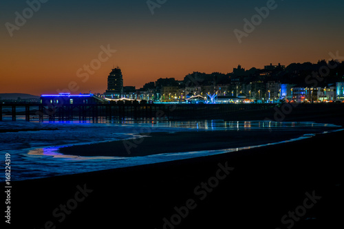 Night scene of Hastings pier and town across the beach at low tide.