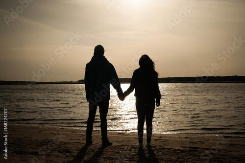 Boy and girl standing in sunset together in hands near river.