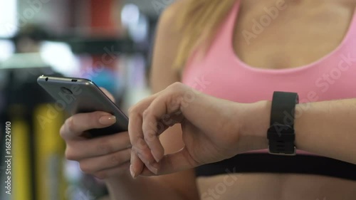 Girl connecting smartphone to her smart watch in gym before sports exercising photo