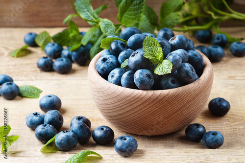 Freshly picked juicy and fresh blueberries with green mint leaves in light wooden bowl on rustic table. Bilberry on horizontal wooden background. Healthy eating and antioxidant nutritions concept.
