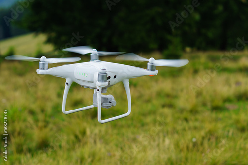 White professional camera drone takes pictures. Professional copter. Horizontal outdoor background, copy space, selective focus. Quadcopter on green grass.