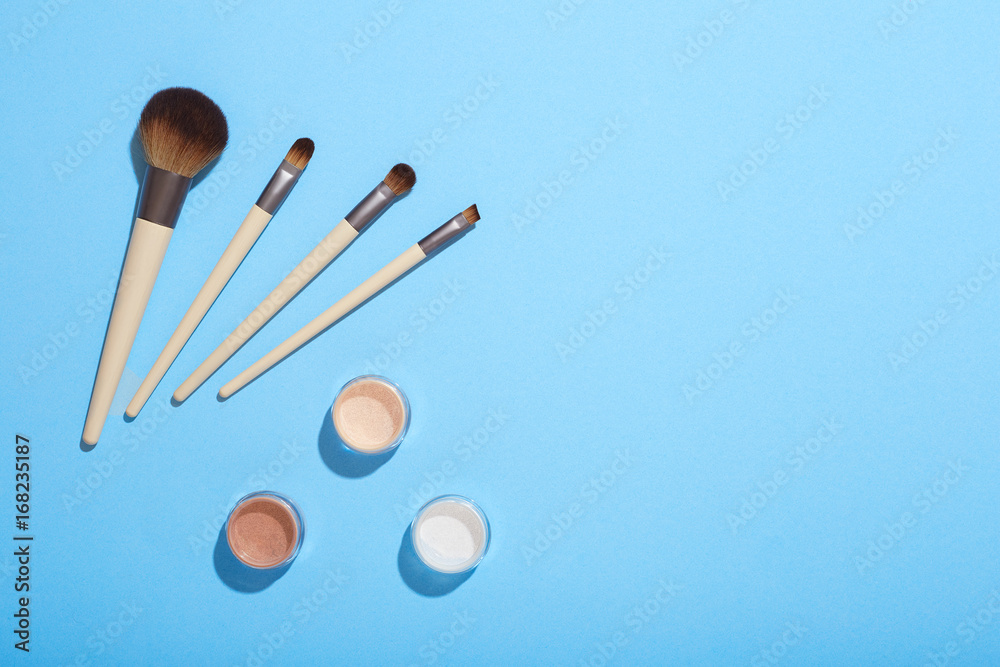 Set of makeup brushes and mineral eye shadows on blue background Set of makeup brushes and mineral eye shadows on blue background