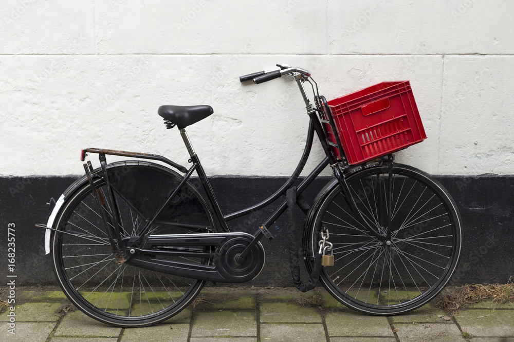 Black bicycle with red basket at white wall Black bicycle with red basket at white wall