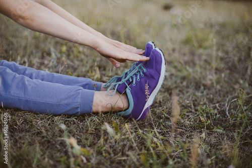 Sport concept,blue sneakers for running  with walkgirlslying on grass. Girl sitting on pitch, no face, legs in professional sport shoes, closeup. Outdoors, sunlight, field