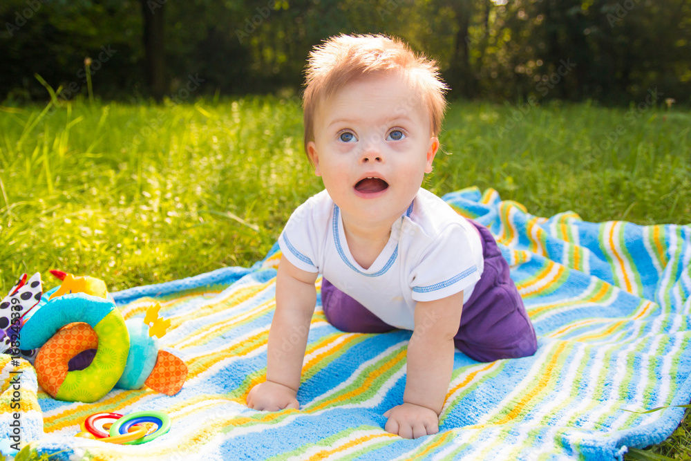 Naklejka premium Portrait of Cute baby boy with Down syndrome lying on blanket in summer day on nature