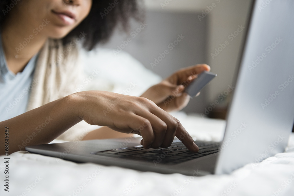 © JGI/Jamie Grill/Blend Images - African American woman laying in bed online shopping with laptop