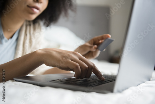 African American woman laying in bed online shopping with laptop