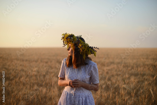 beautiful girl in wreath of flowers in meadow on sunny day. Portrait of Young beautiful woman wearing a wreath of wild flowers. Young pagan Slavic girl conduct ceremony on Midsummer. Earth Day