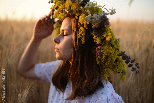 beautiful girl in wreath of flowers in meadow on sunny day. Portrait of Young beautiful woman wearing a wreath of wild flowers. Young pagan Slavic girl conduct ceremony on Midsummer. Earth Day