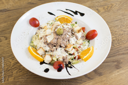 Tuna salad with lettuce, olives, and tomatoes. Orange decoration on a white plate.