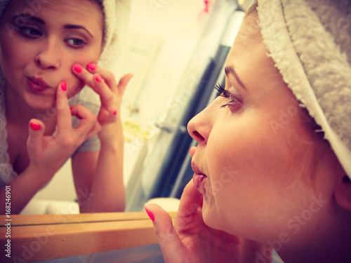 Bilde på lerret Woman looking in mirror dealing with acne