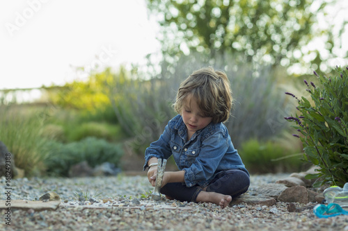Caucasian boy sitting on ground smashing rocks with hammer