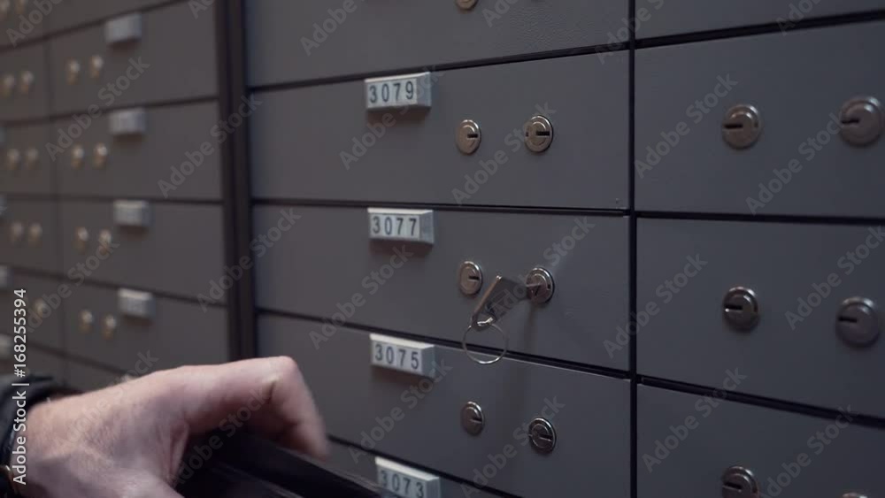 Unrecognisable old man hands with wedding ring on finger puts plastic case inside bank safe depository cell