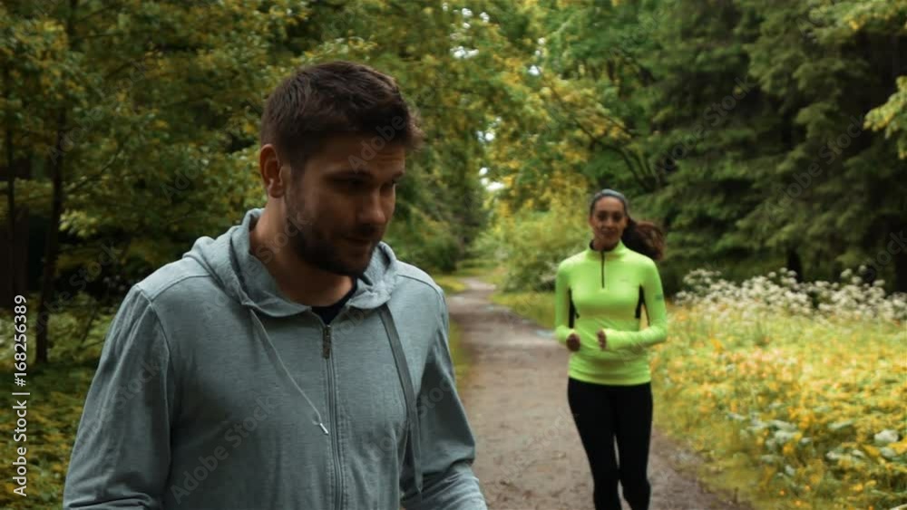 Young attractive successful runner guy winner run with woman loser falls behind in park. Super slow motion shot stabicam. Young attractive successful runner guy winner run with woman loser falls behind in park. Super slow motion shot stabicam.