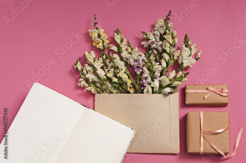 Flowers composition. Gifts, copybook and heart shaped flowers in envelope on pink background. Flat lay, top view.