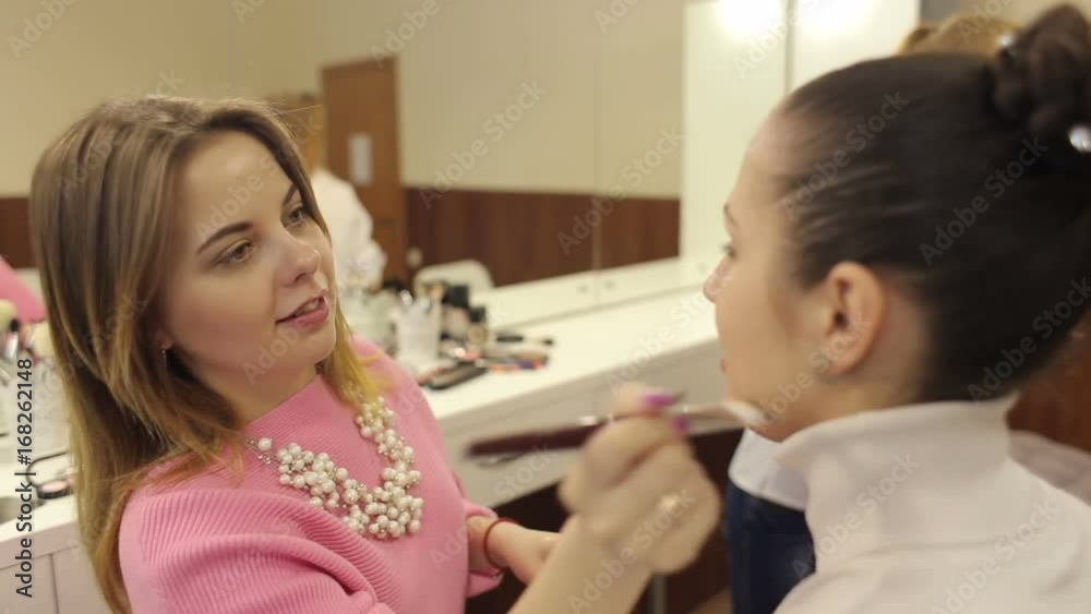 Young woman applying makeup to model in beauty salon. Make-up artist at the work with client. Make-up artist working in a crowded beauty salon. Young woman applying makeup to model in beauty salon. Make-up artist at the work with client. Make-up artist working in a crowded beauty salon.