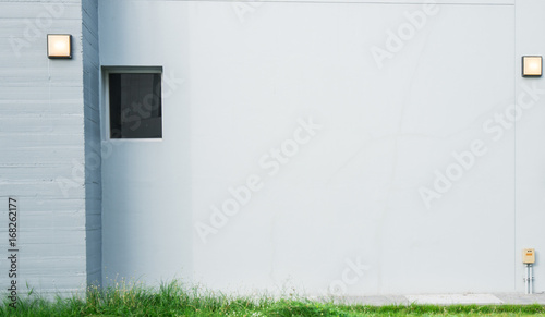 Grey concrete wall with lamp and have green grass at the bottom