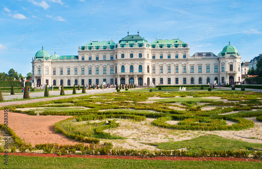 Naklejka premium Close view on magnificent Belvedere palace surrounded by a beautiful trimmed flowerbed and lawn against a blue vibrant sky with several solitary clouds. Summer, Vienna