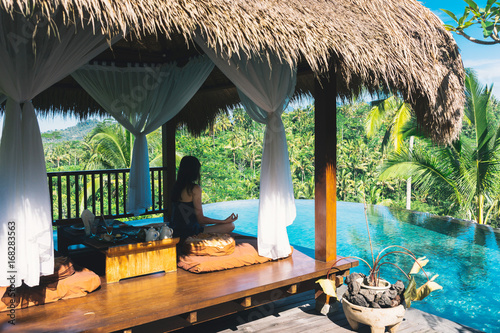 Girl meditating by the pool on a background of palms, Bali, Indonesia.The girl sits in a gazebo at a bali in a lotus pose and meditates with a view of the palms and the pool. Breakfast in Bali photo